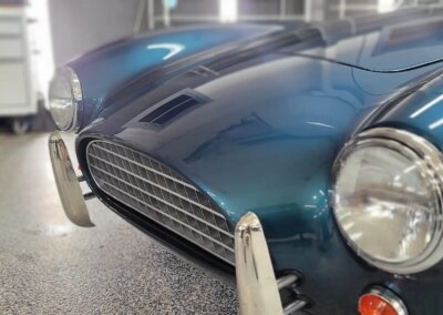 A black car being detailed by a worker using a polishing machine.
