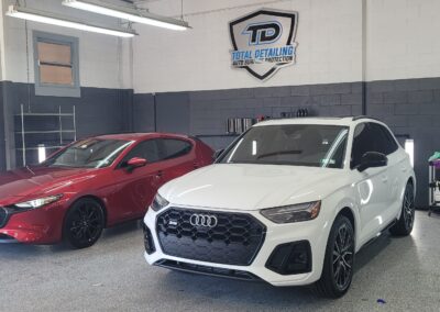 A car with shiny red paint being detailed by a professional with a microfiber cloth.