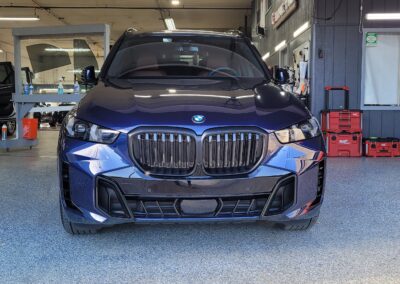 A car with a glossy finish being detailed by a worker in protective gear.