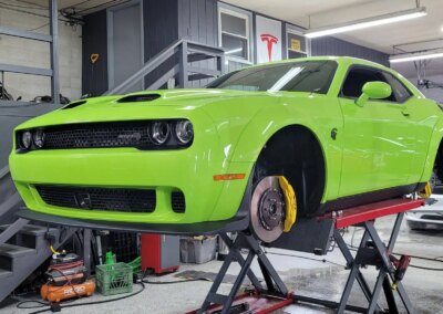 A detailing technician polishing a black car's hood with a power buffer.