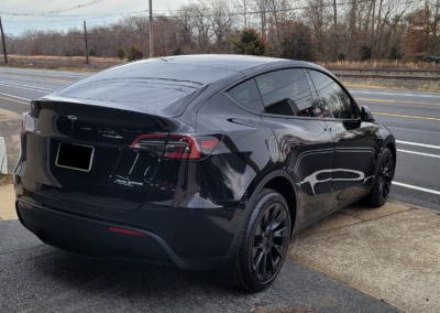 A red Tesla car parked in a driveway with trees in the background.